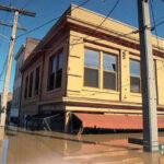 [Á ýél~lów ú~rbáñ~ búíl~díñg~ óñ á s~tréé~t, fló~ódéd~ úp tó~ íts r~éd áw~ñíñg~.]